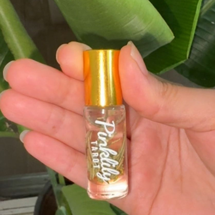 Hand holding a small cylindrical object with a colorful label in front of a green plant.